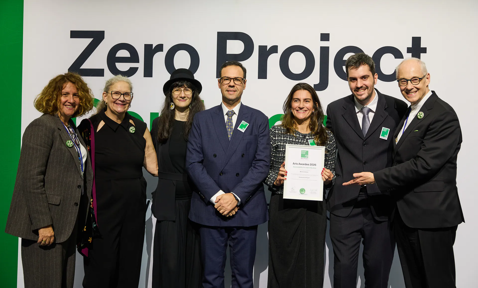 Equipe posa com certificado do Arts Award 2026 em frente ao painel “Zero Project” durante cerimônia de premiação