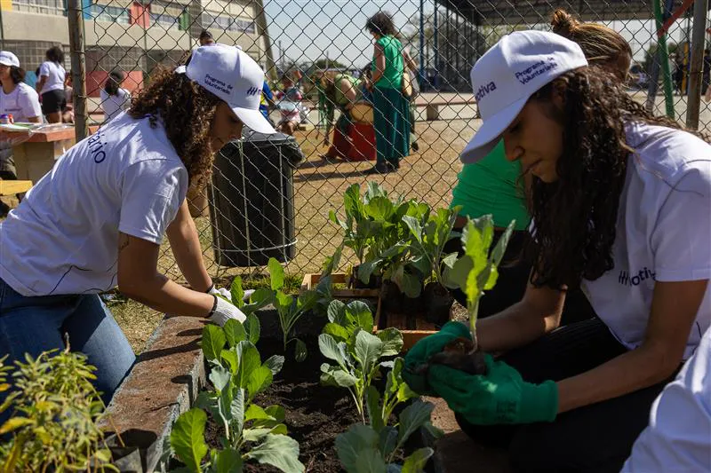  Colaboradoras da Motiva plantando mudas em uma horta comunitária durante ação solidária ao ar livre.