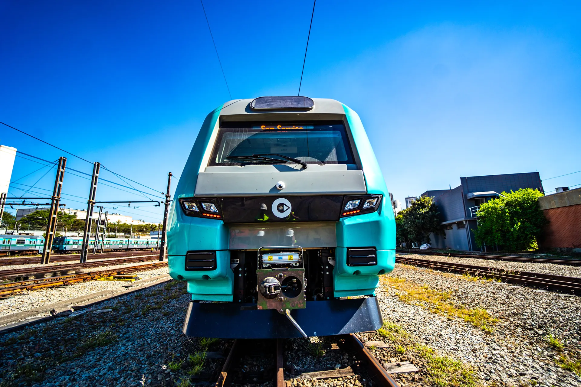 Trem moderno de cor turquesa da ViaMobilidade posicionado em trilhos ferroviários sob céu azul.