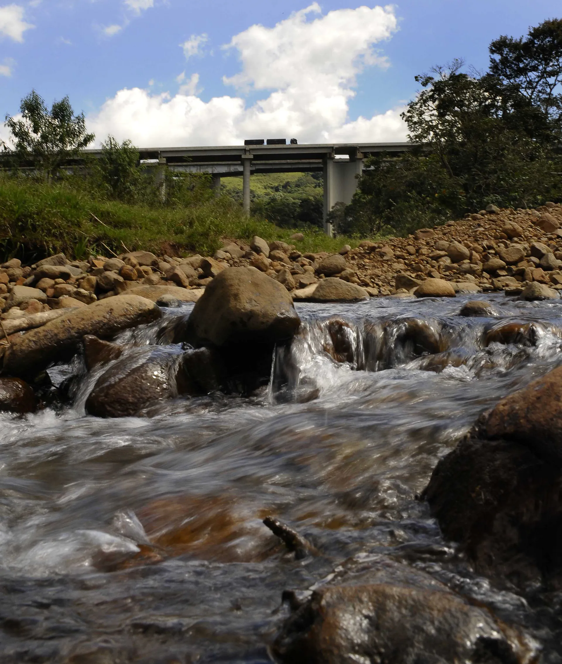 Pedras marrons em um riacho com uma ponte ao fundo