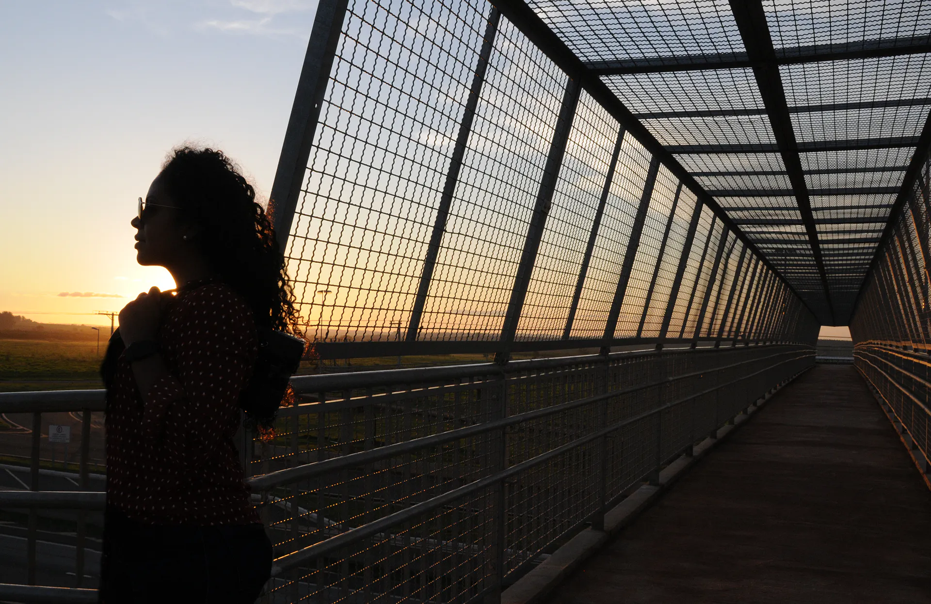 Mulher observando o horizonte com uma passarela de pedestres ao fundo