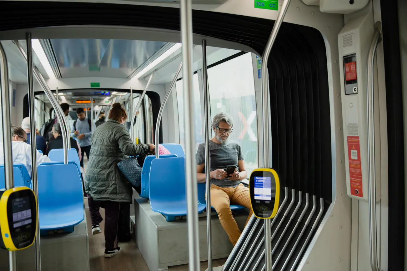 Homem sentado em um banco de metrô enquanto outras pessoas ao fundo se acomodam no vagão