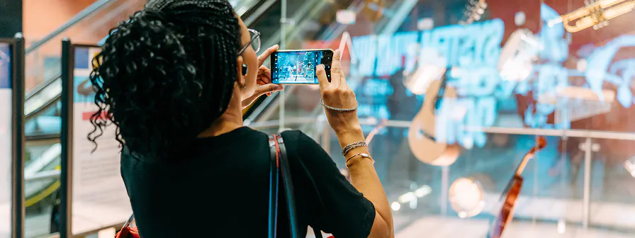 Mulher tirando foto com celular em frente à escada rolante em uma estação de metrô