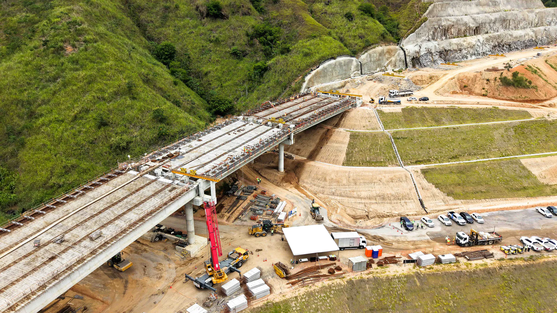 Imagem aérea mostra construção de uma rodovia com operários e frota de veículos
